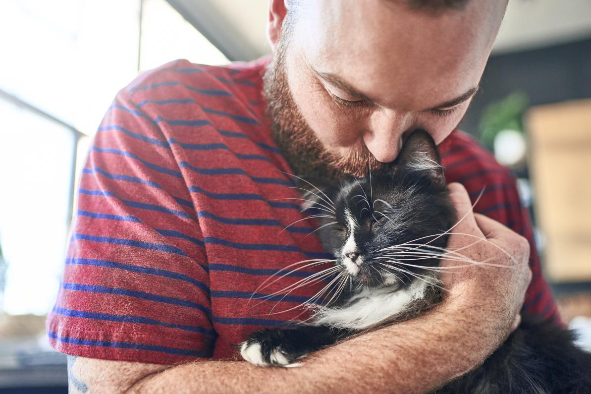 Adult male pet owner hugging his black and white cat